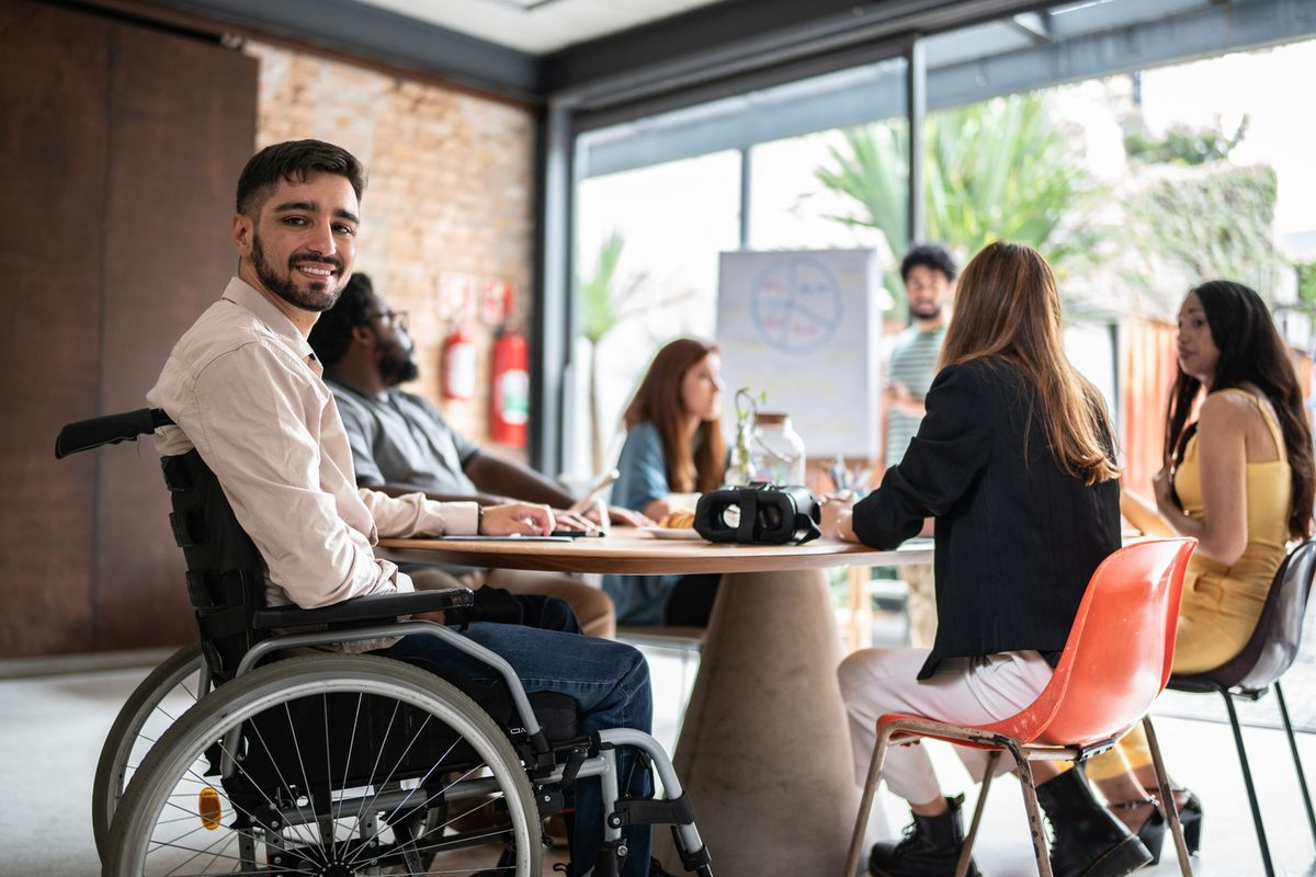 Smiling young man using a wheelchair at a table with a diverse group of people in a bright community space